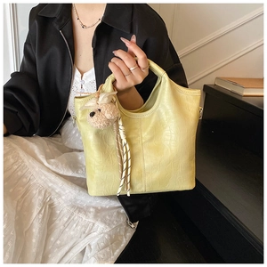 Detail of lime yellow crocodile leather handbag with a cute plush bear pendant accessory