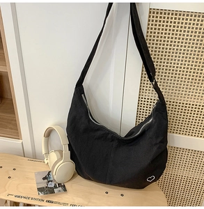 Detail of black canvas hobo bag featuring a minimalist white heart embroidery and silver zip