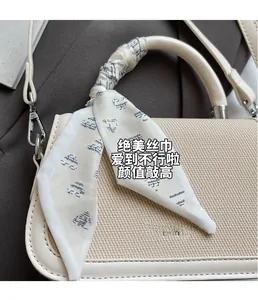 Detail of cream-colored crossbody bag with woven texture and decorative silk scarf handle