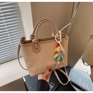 Detail of straw woven bucket bag with brown leather trim and cute doll pendant charm