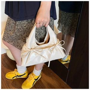 Detail of a creamy beige patent leather handbag featuring decorative bow ties on the front
