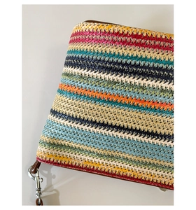 Detail of colorful striped woven bag with brown leather trim and silver metal buckle
