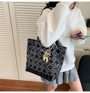 Detail of a large black tote bag with geometric patterns and cute doll charm accessory
