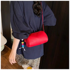 Detail view of a red lychee pattern cylinder crossbody bag with letter bead charm