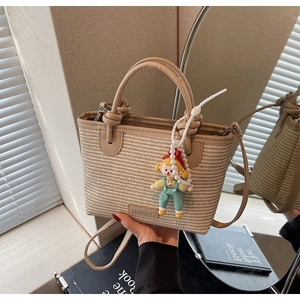 Detail of woven straw bucket bag with leather handle and pearl charm in warm lighting