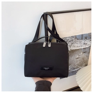 Détail du sac à bandoulière en nylon noir avec écusson logo et fermeture éclair argentée