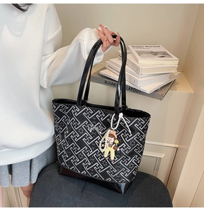 Detail of black tote bag featuring geometric patterns, leather handles and doll charm