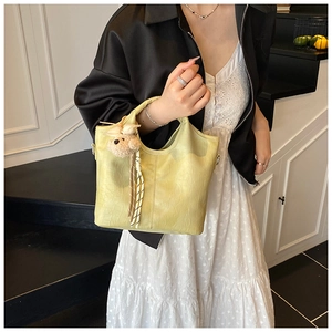 Detail of pale yellow bucket bag with crocodile embossing and plush bear charm