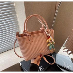 Detailed close-up of pink woven bucket bag with pearl doll charm and metal logo plate