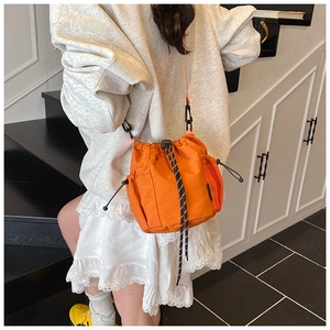 Detail of vibrant orange drawstring bucket bag with black and white woven rope accent