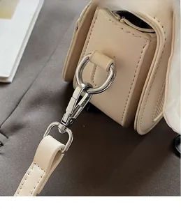 Detailed close-up of silver metal hook and beige leather shoulder strap on handbag
