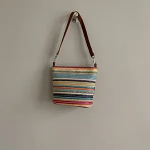 Detail of multi-color striped woven texture and brown leather strap on shoulder bag