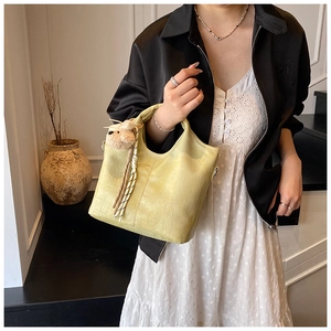 Detail of pale yellow crocodile texture bucket bag with plush bear charm and tassel charm