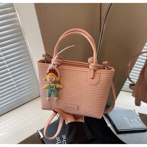 Detail shot of a pink woven bucket bag with leather handles and a cute cartoon charm