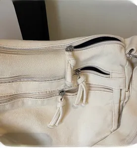 Detail of smooth silver zippers and multi-pocket design on beige canvas shoulder bag