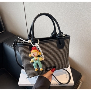 Detail of woven bucket bag with leather handle and cute doll charm on art books
