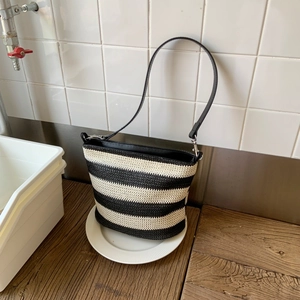 Detailed texture of black and white striped woven bucket bag with faux leather strap