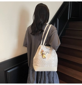 Detail view of white geometric bucket tote bag with metal bow and yellow doll charm