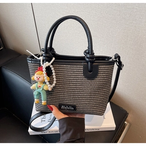 Detail of woven straw bucket bag with leather handles and pearl doll charm accessory