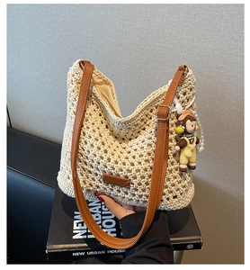Detail of woven tote bag with brown leather straps, pearl chain, and cartoon charm