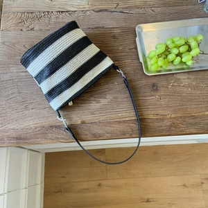 Close-up of woven black and white striped tote bag with leather strap on a wooden table