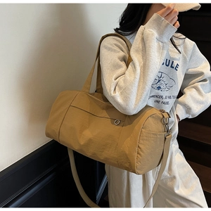 Khaki cylindrical nylon travel bag shown on shoulder with adjustable strap and metal buckle