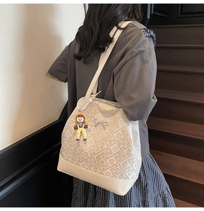 Detail of beige tote bag with geometric woven pattern, silver bow charm and doll pendant