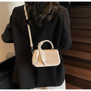 Beige crossbody bag with silk scarf on handle held by model on wooden stairs
