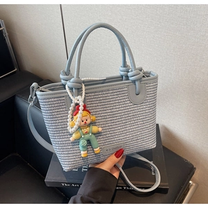 Close-up of light blue woven straw bucket bag with cute doll charm and crossbody strap