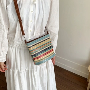 Detail of multi-colored striped woven bag with brown leather strap and metal hooks
