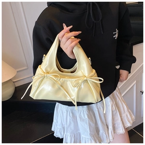 Detail showing light yellow glossy mini handbag with side pleats and bow decoration