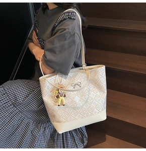 Close-up of beige woven tote bag featuring metal bow and cute cartoon pendant detail