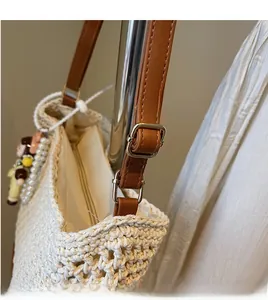 Detail of woven tote bag showing adjustable brown leather strap and decorative charms
