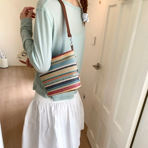 Detailed view of colorful striped woven tote bag with brown leather shoulder strap