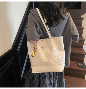 Detailed view of beige jacquard tote bag with bow charm and doll on model's shoulder