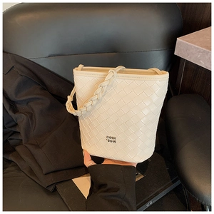 Detail of cream woven bucket bag showing premium leather texture and metal logo