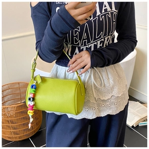Dettaglio borsa a cilindro verde frutta con trama litchi e ciondolo di perline colorate