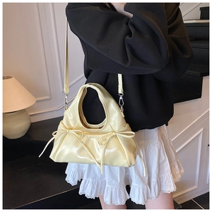 Detail of cream-colored shoulder bag with bows and elegant cloud pleats worn by model