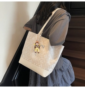 Close-up of beige tote bag featuring geometric patterns and a cute character pendant