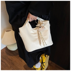 Detailed close-up of white crocodile pattern bucket bag with plush bear charm accessory