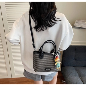 Detail of woven bucket bag with leather trim and cute doll charm worn crossbody
