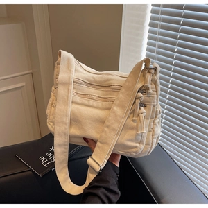 Detail of cream canvas crossbody bag with multiple zipper pockets and adjustable strap