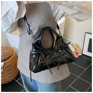 Close-up of black patent leather bag featuring elegant bow knots and pleated texture
