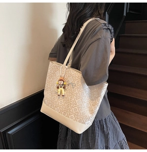 Detail of cream tote bag featuring embossed floral patterns and silver bow charm accent