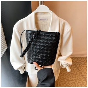 Detail of black woven bucket bag with metal logo and drawstring liner against white suit