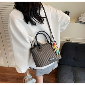 Detail of grey woven bucket bag with pearl doll charm and detachable black strap