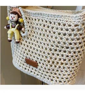 Detail of crochet tote bag featuring brown leather tag and pearl pendant accessory