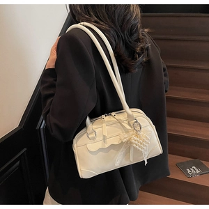 Detail of cream white glossy pillow bag with pearl and lace bow charm on model's shoulder