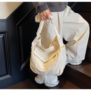 Detail of off-white canvas tote bag featuring front flap pocket and wide shoulder strap