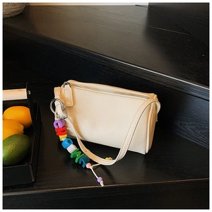 Close-up of beige lychee texture cylinder crossbody bag with colorful letter charm